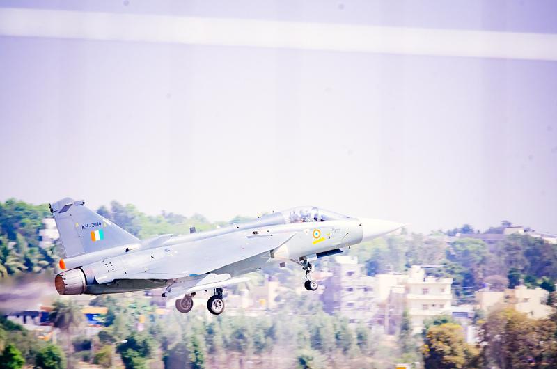 Tejas lifting off with its landing gear still extended, buildings behind