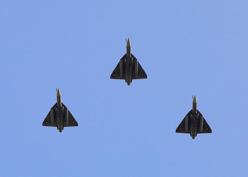 Three Tejas seen from below in a tight vic formation against a blue sky